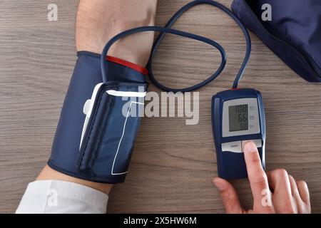 Uomo che prende la pressione sanguigna con un misuratore digitale su un tavolo di legno a casa. Vista dall'alto. Foto Stock