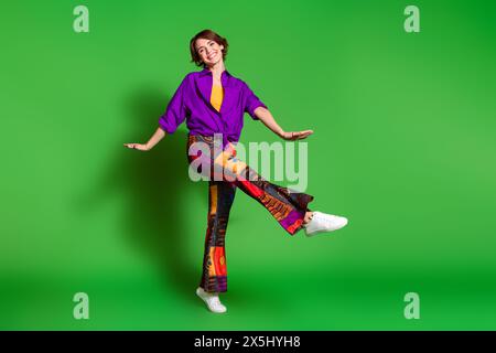 Ritratto fotografico di una giovane donna divertente con elegante camicia viola e taglio di capelli marrone che balla con libertà isolata su sfondo di colore verde Foto Stock