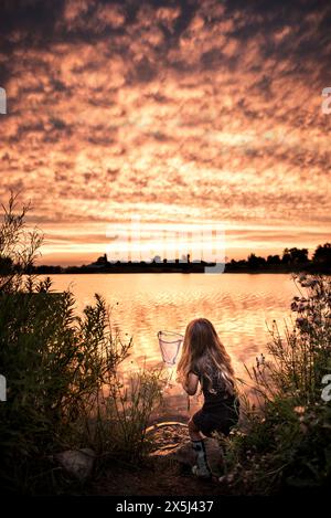 Una ragazza che pesca al bellissimo lago al tramonto Foto Stock