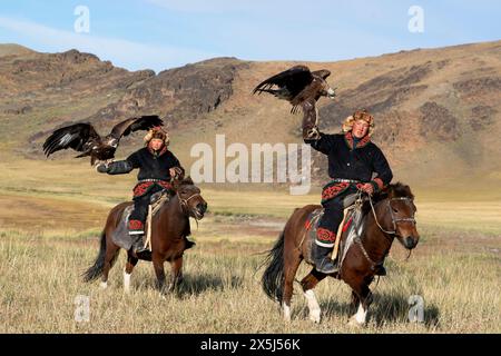 Asia, Mongolia, provincia di Bayan-Olgii. Altai Eagle Festival, due giovani cacciatori di aquile kazaki cavalcano mentre espongono le loro aquile d'oro. (Uso editoriale o Foto Stock