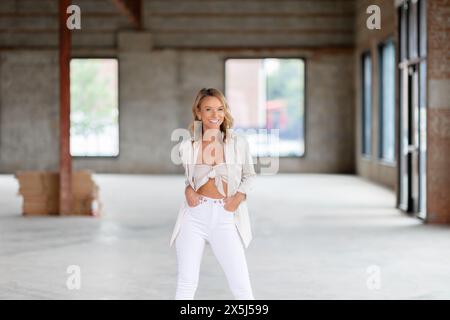 Donna sicura di sé che sorride in tuta bianca in magazzino Foto Stock