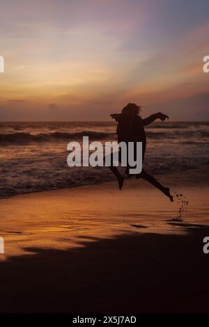 Giovane donna che salta al tramonto sull'oceano, sulla spiaggia. Foto Stock