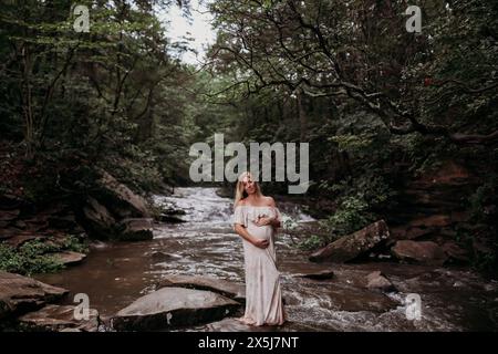 Donna incinta del terzo trimestre in piedi nel fiume Foto Stock
