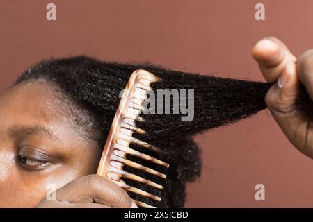 Pettinare i capelli neri ricci con restringimento, utilizzando un pettine a denti larghi per deformare i capelli di tipo 4c bagnati Foto Stock