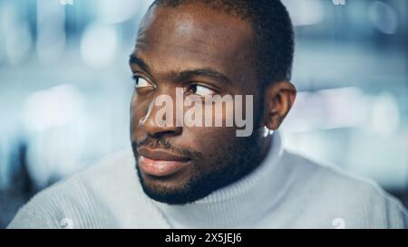 Primo piano Ritratto di bell'uomo nero con occhi marroni profondi, barba rifinita, elegante dolcevita bianco, Winks e Shows Perfect Smile. L'attraente e autentico gentiluomo si trasforma. Foto Stock