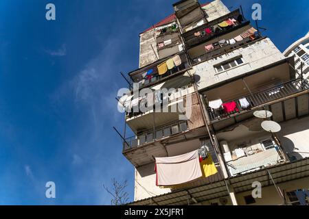 Vecchia casa a più piani con piatti satellitari e balconi con vestiti asciuganti su uno sfondo blu del cielo. Foto dal basso verso l'alto Foto Stock