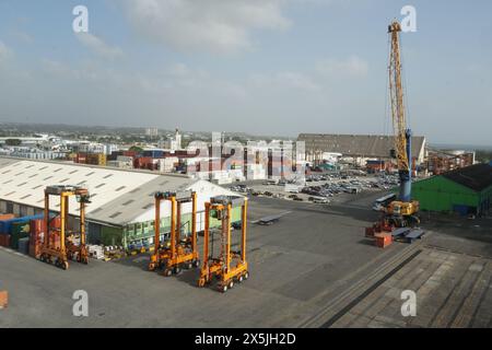 Nel terminal container di Bridgetown, tre portacontainer arancioni sono parcheggiati vicino a un magazzino e a una gru mobil. Foto Stock