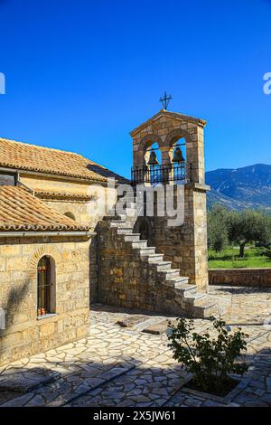 Grecia. Chiesa greca in pietra con tetto piastrellato, finestre ad arco, campanile e un uliveto Foto Stock