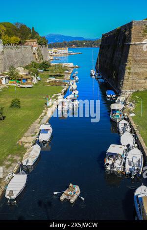 Corfù, Grecia. La città fortificata di Corfù, il canale della fortezza con barche, la persona che canta una zattera e un parco Foto Stock