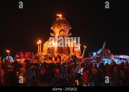 Vivace scena notturna del Desert Music and Art Festival, installazione artistica stravagante e partecipanti incandescenti Foto Stock