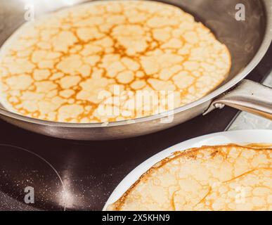 Primo piano dei pancake fritti in una padella in acciaio inossidabile accanto ai pancake già pronti. Ricetta di crepe suzette. Messa a fuoco selezionata. Foto di alta qualità Foto Stock