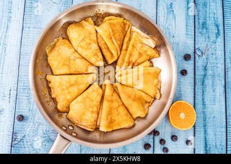 Pancake crepe suzette in una padella su un tavolo di legno. accanto all'arancia tagliata in padella e ai mirtilli. Foto di alta qualità Foto Stock