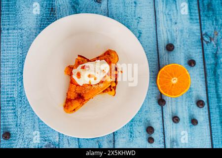 Frittelle su un piatto bianco con gelato e salsa d'arancia, vista dall'alto. Crepe suzette accanto a un'arancia tagliata e frutti di bosco. Foto di alta qualità Foto Stock