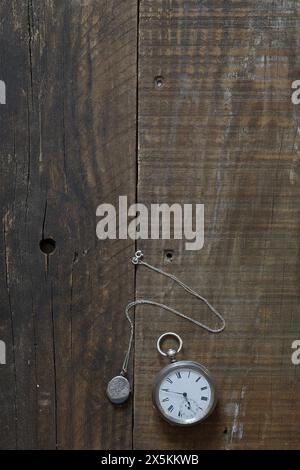 Un vecchio orologio da tasca in argento e un ciondolo d'argento adagiato su vecchie tavole di legno e sul piano del tavolo. copertina libro still life style. Foto Stock