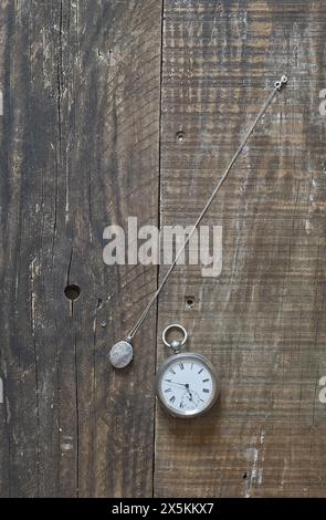 Un vecchio orologio da tasca in argento e un ciondolo d'argento adagiato su vecchie tavole di legno e sul piano del tavolo. copertina libro still life style. Foto Stock