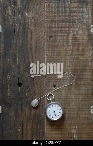 Un vecchio orologio da tasca in argento e un ciondolo d'argento adagiato su vecchie tavole di legno e sul piano del tavolo. copertina libro still life style. Foto Stock