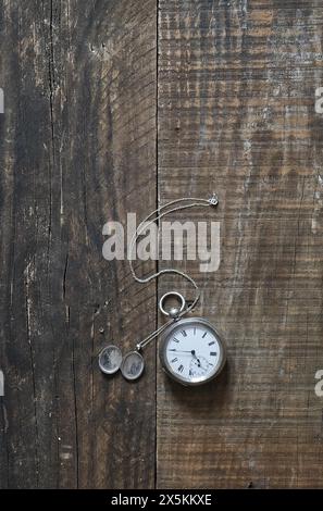 Un vecchio orologio da tasca in argento e un ciondolo d'argento adagiato su vecchie tavole di legno e sul piano del tavolo. copertina libro still life style. Foto Stock