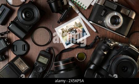 Vista dall'alto della fotografia di una giovane donna che scatta una foto, circondata da flash, filtri, obiettivi, fotocamere moderne e vecchie su un tavolo di legno Foto Stock