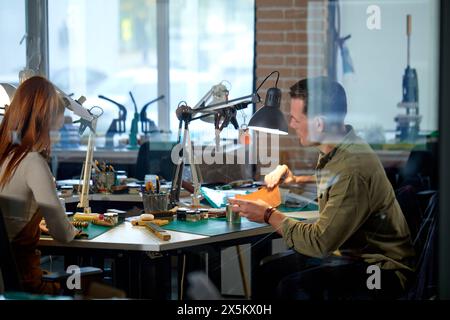 giovane artigiana attiva che lavora in officina, dietro una parete di vetro. hobby, stile di vita. lavoro, professione. Foto Stock