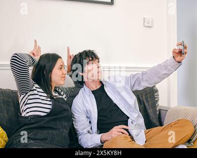 Fratello e sorella seduti sul divano a fare selfie Foto Stock