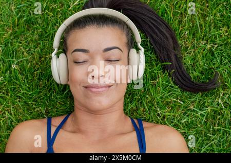 Donna con le cuffie stesa sull'erba Foto Stock