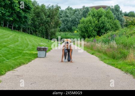 Donna con cuffie accovacciate sul percorso, pronta per correre Foto Stock