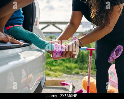 Madre che mette le scarpe di gomma sulla figlia Foto Stock