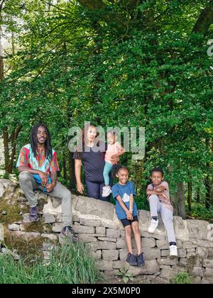 Famiglia con bambini seduti su un muro di pietra Foto Stock