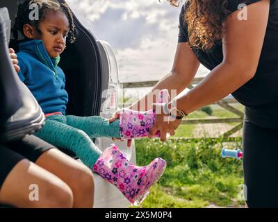 Madre che mette le scarpe di gomma sulla figlia Foto Stock