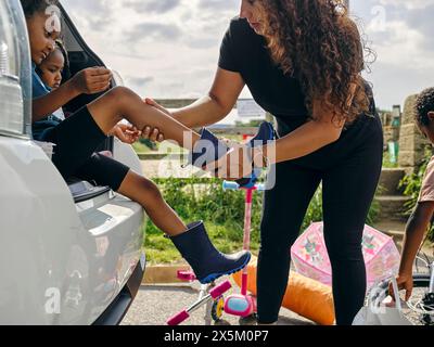 Madre che mette scarpe di gomma sui bambini Foto Stock