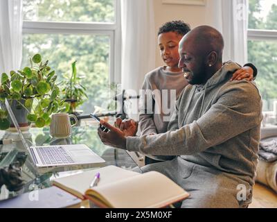 Padre e figlio che usano il telefono e il portatile a casa Foto Stock