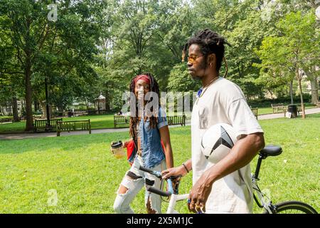 USA, giovani alla moda che camminano sul prato nel parco con la bicicletta Foto Stock