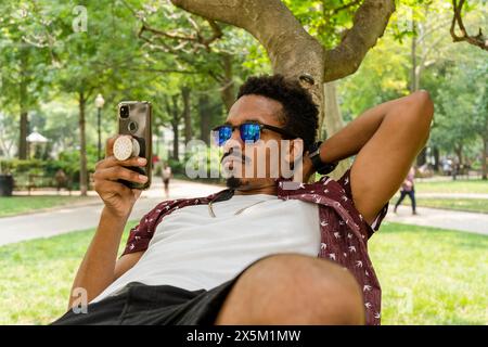 USA, uomo con smartphone sdraiato sul ramo dell'albero nel parco Foto Stock