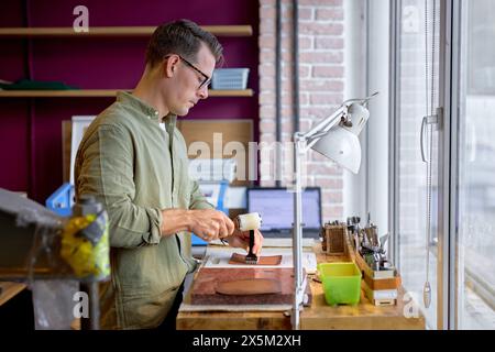 Artigiano di successo che utilizza il punzone e il martello, foto da vicino con vista laterale, lavoro, tempo libero, tempo libero, stile di vita Foto Stock