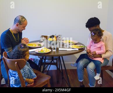 Famiglia con figlie che prega prima di mangiare Foto Stock