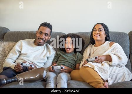 Ragazzo che gioca a videogame con madre e padre con protesi alla gamba Foto Stock