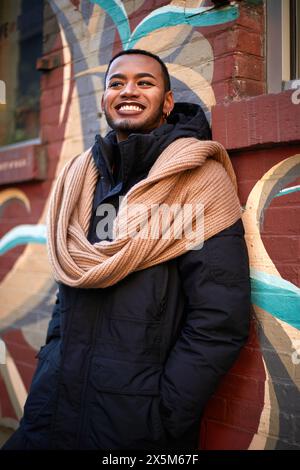 USA, New York City, Ritratto di uomo queer sorridente in giacca e sciarpa Foto Stock