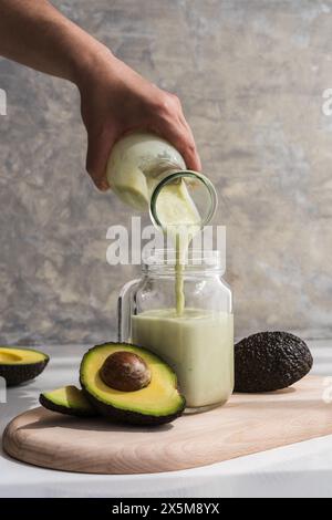 versare a mano un frullato di avocado in una caraffa di vetro utilizzando una bottiglia di vetro Foto Stock