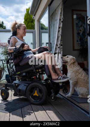 Donna in sedia a rotelle elettrica che si rilassa sul ponte con il cane Foto Stock