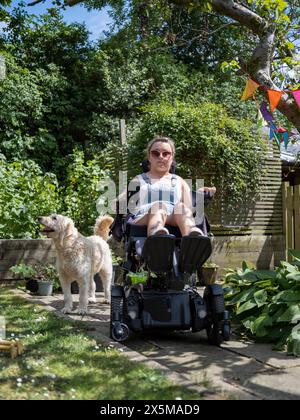 Donna in sedia a rotelle elettrica con cane nel cortile posteriore Foto Stock