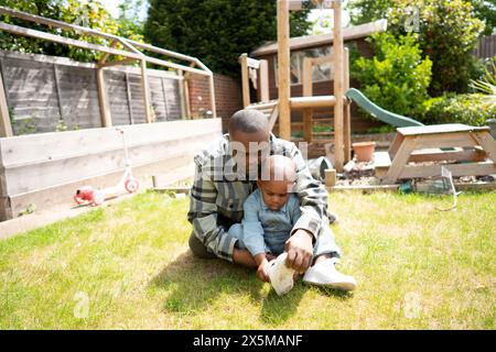 Padre con sindrome di Down che aiuta figlio (2-3) indossare la scarpa Foto Stock