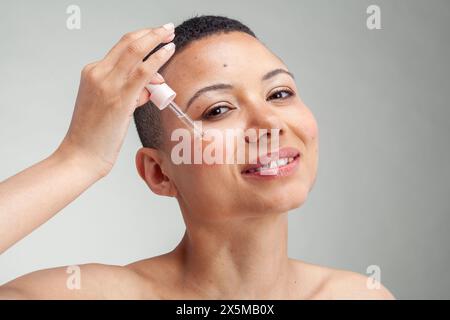 Ritratto di donna sorridente che applica siero sulla guancia Foto Stock