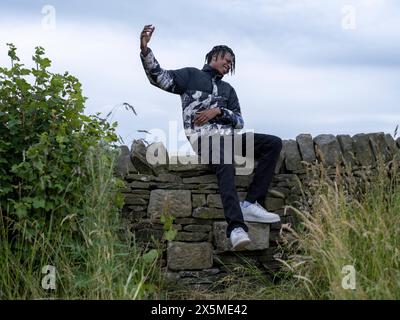 Giovane seduto su un muro di pietra Foto Stock