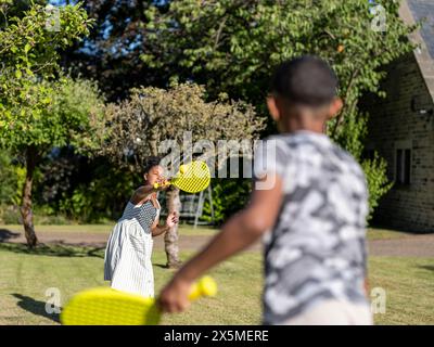 Fratelli (8-9, 10-11) che giocano a paddle ball in giardino Foto Stock