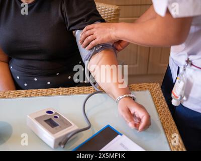 Infermiera che misura la pressione sanguigna di una donna matura Foto Stock