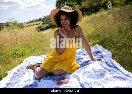 Giovane donna seduta su una coperta nel prato Foto Stock