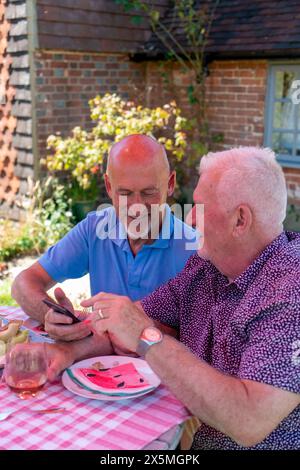 Coppia di uomini anziani che si rilassano in giardino e utilizzano il telefono Foto Stock