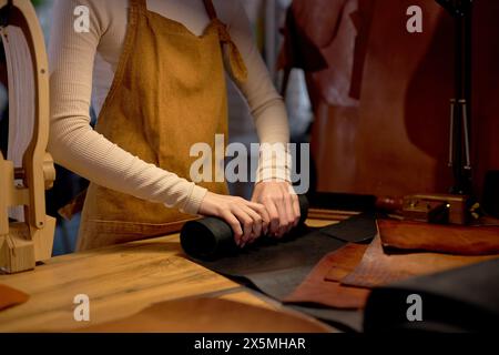 sarta esperta che sfoggia un rotolo di pelle sul tavolo in officina a casa.primo piano con vista laterale ritagliata Foto Stock