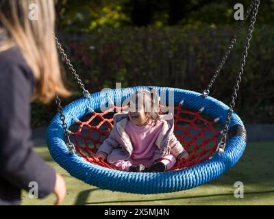 Madre e figlia con sindrome di Down che usano l'altalena sul parco giochi Foto Stock