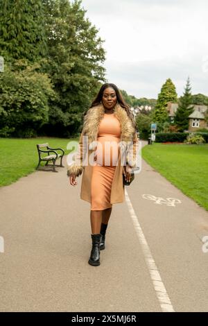 Ritratto di donna incinta in cappotto che cammina nel parco in autunno Foto Stock